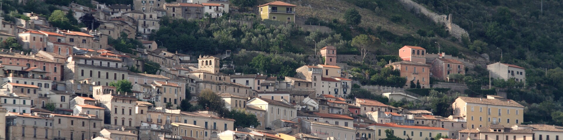 Un pueblo en una ladera con muchas construcciones históricas y colinas boscosas al fondo.