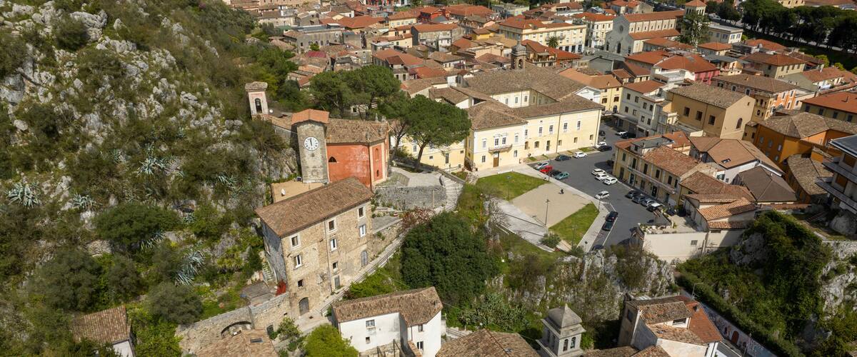 An aerial view of a historic town with terracotta-roofed buildings, a prominent church, and lush greenery.