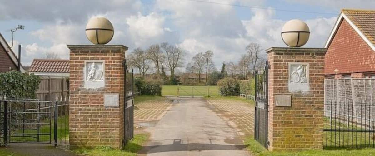 A paved pathway leading to a gated entrance with brick pillars and spherical decorations.