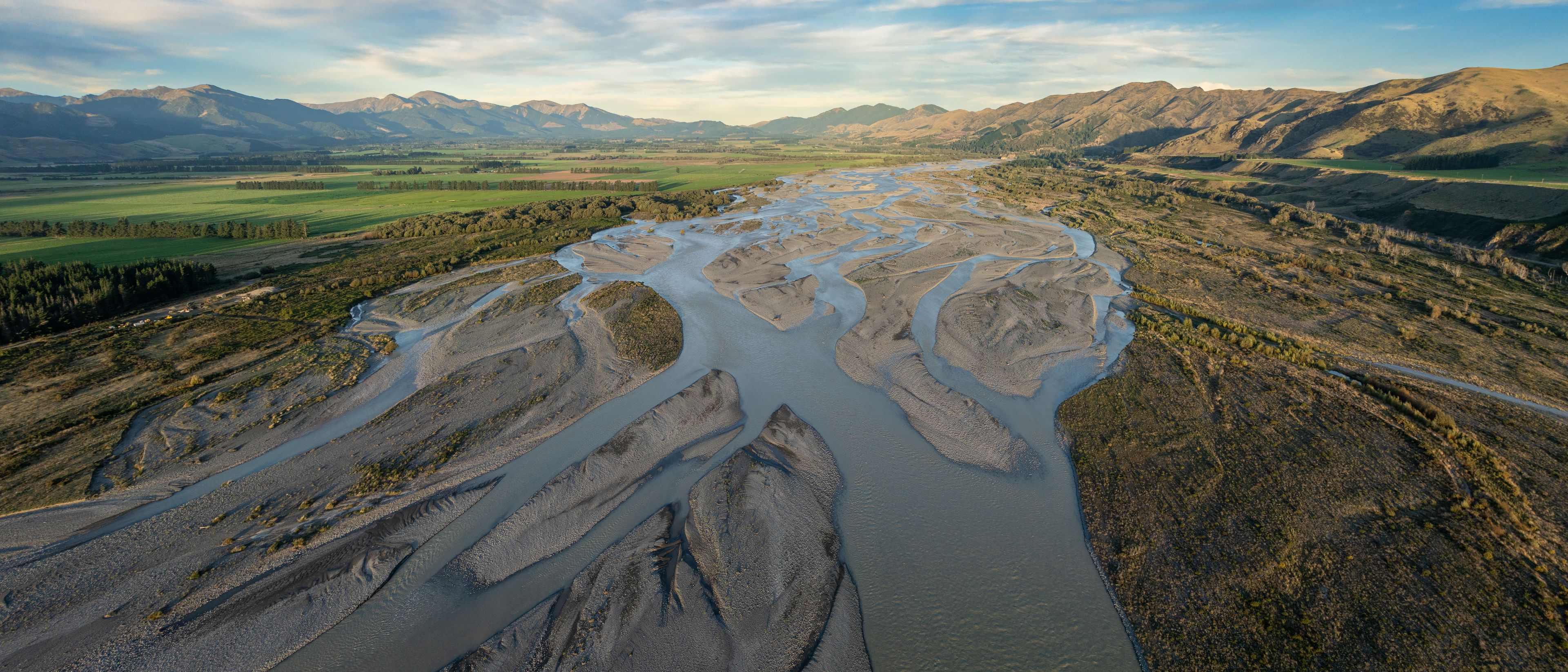 Un río serpentea a través de un paisaje montañoso con campos verdes y montañas al fondo.