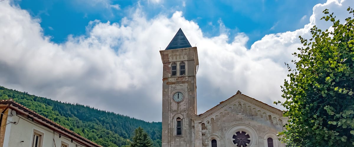A historic church with a clock tower, surrounded by buildings and greenery.