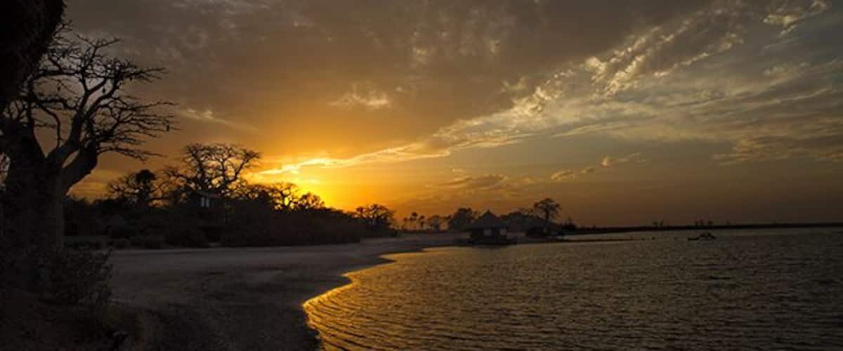 A sunset over a river with a tree on the left and a boat in the water.