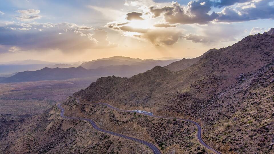 A winding mountain road with a view of distant mountains and a cloudy sky.