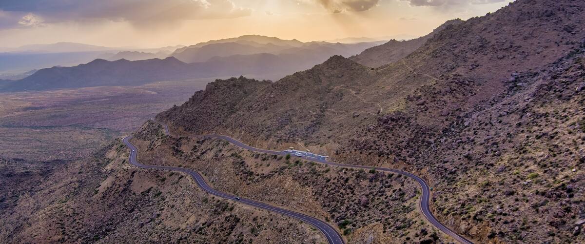 A winding mountain road with a view of distant mountains and a cloudy sky.