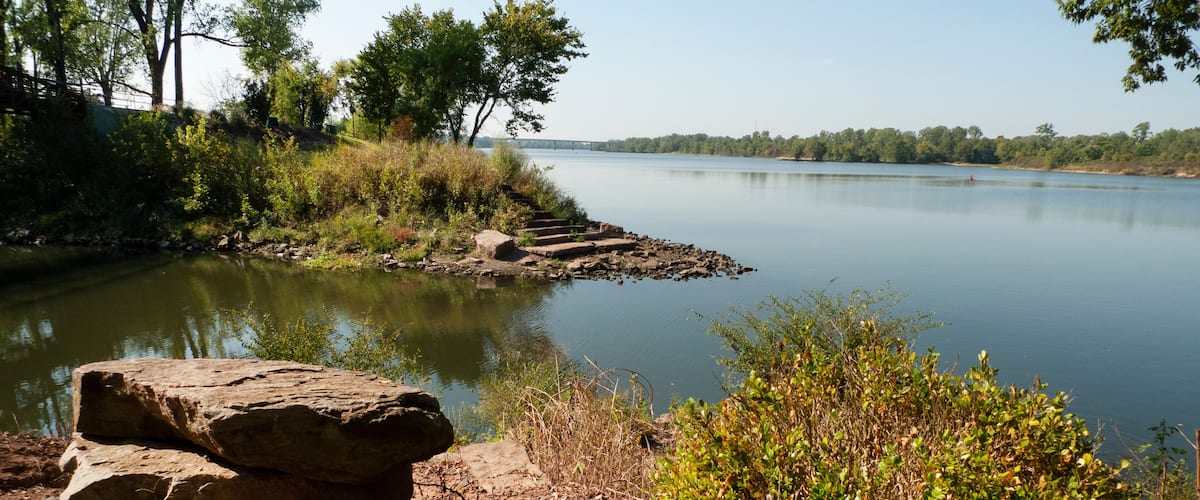 A calm lake with a rocky shore, surrounded by trees and bushes.