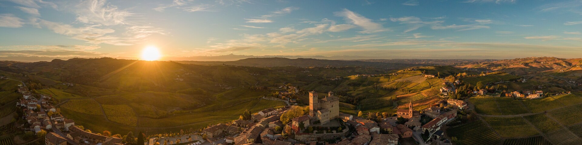 Vista panorámica de un pueblo histórico con un castillo imponente, rodeado de colinas ondulantes y viñedos.