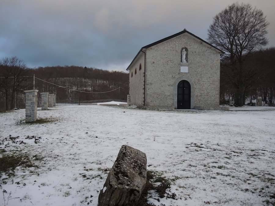 Una iglesia de piedra con un campo nevado y árboles desnudos al fondo.