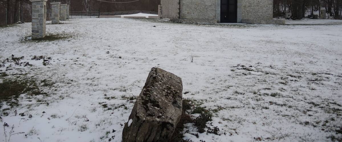 A stone church with a snow-covered field and bare trees in the background.