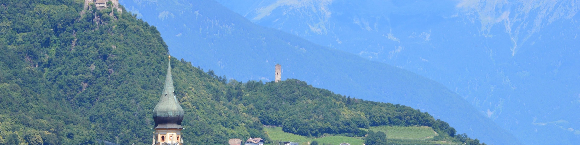 A mountainous landscape with a church tower, houses, and a castle on a hill.