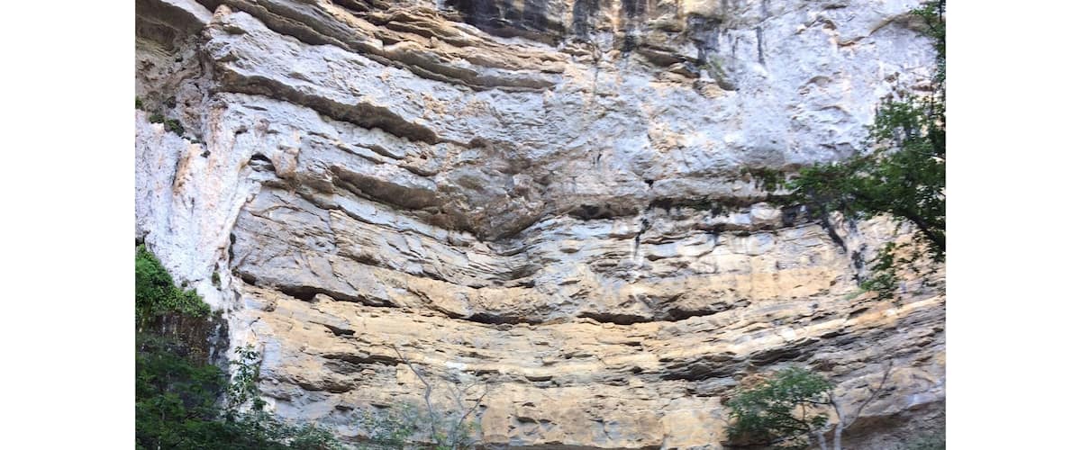 A layered rock formation with a person standing at the bottom.