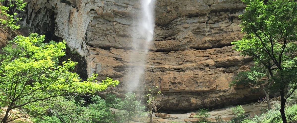 Hemmed-in Hollow is one of the beautiful waterfalls located in the Buffalo River Wilderness Area.  
This towering waterfall is best accessed from the river.  The trail is located between Steele Creek and Kyle's Landing, both popular camp areas and river access points along the Buffalo National River.  I don't think the trail is marked, but it's not a secret and there are usually plenty of people who can guide you on where to stop.  It's about a 1.5 mile trip each way with a little elevation gain...but not a difficult hike.
You can reach Hemmed-in Hollow over land, but that is a more strenuous hike.