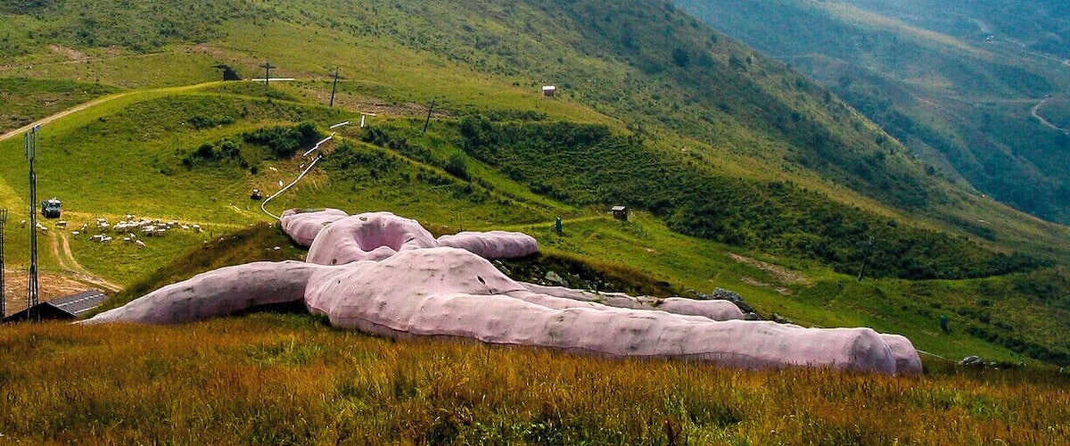 A large pink sculpture in a grassy field with mountains in the background.