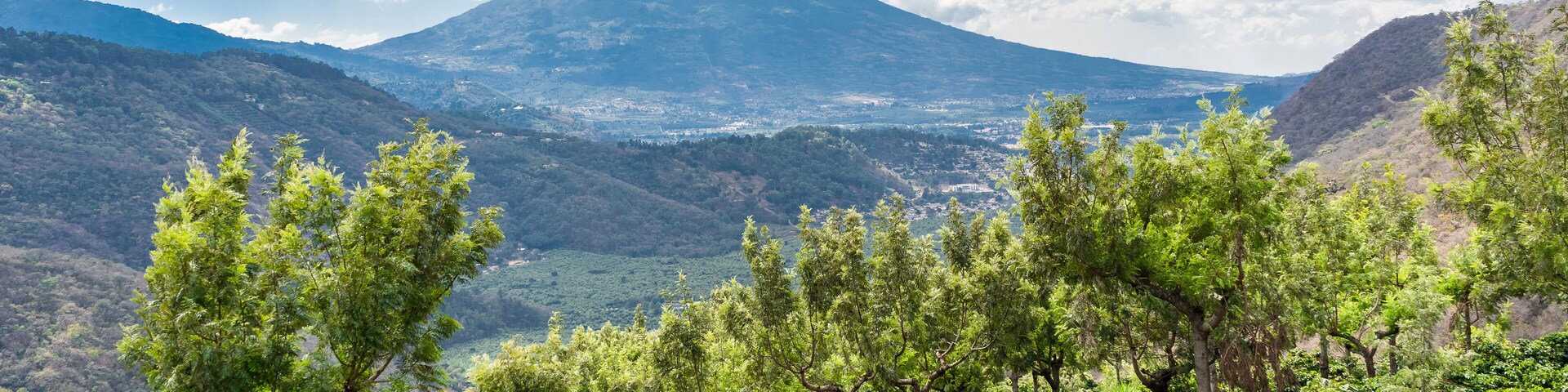 Un paisaje montañoso con vegetación exuberante y una vista de un volcán distante.