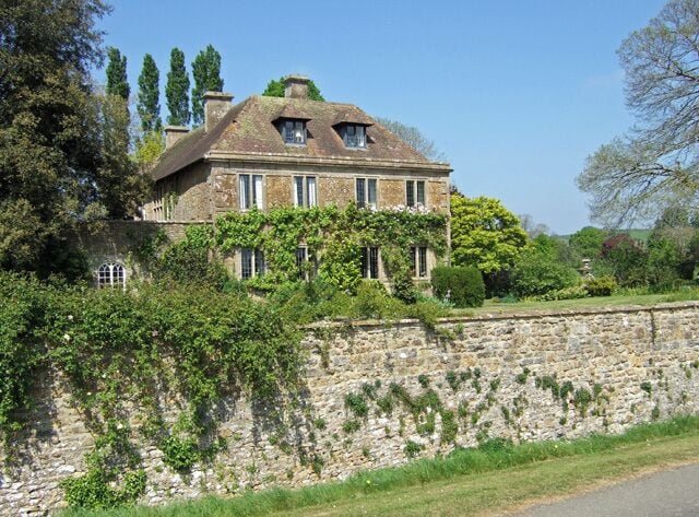 A stone wall with a large house behind it.
