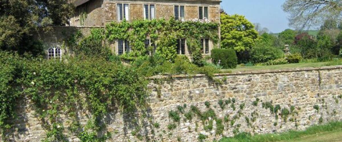 A stone wall with a large house behind it.