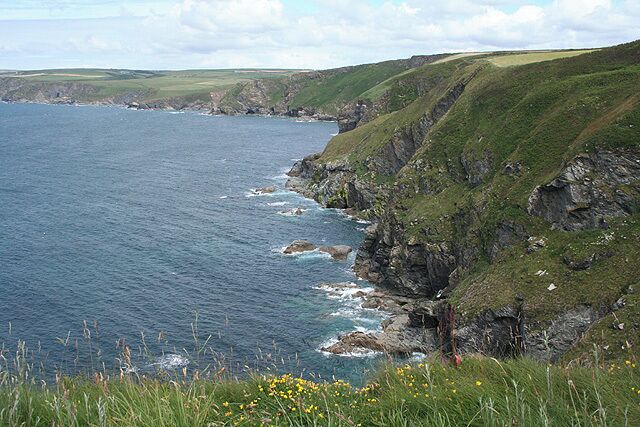 Un paisaje costero con acantilados, laderas cubiertas de hierba y el mar.
