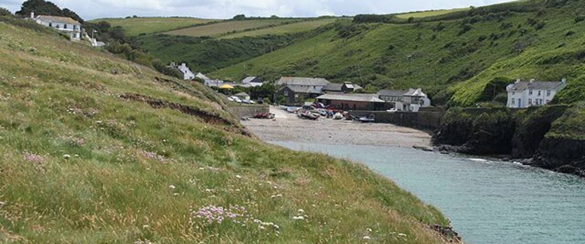 Un pueblo costero con casas en una colina, una playa y un mar tranquilo.