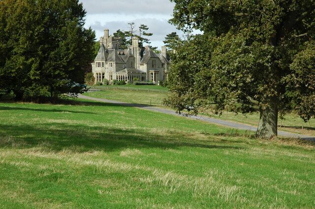 A large, historic house with a well-maintained lawn and trees in the foreground.