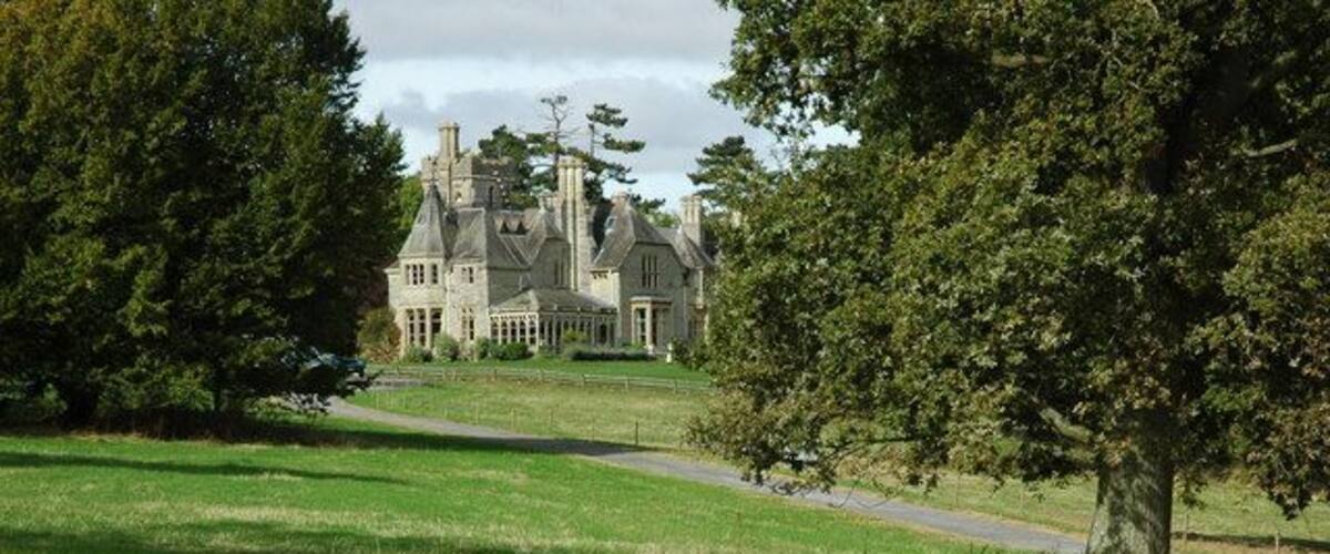 A large, historic house with a well-maintained lawn and trees in the foreground.