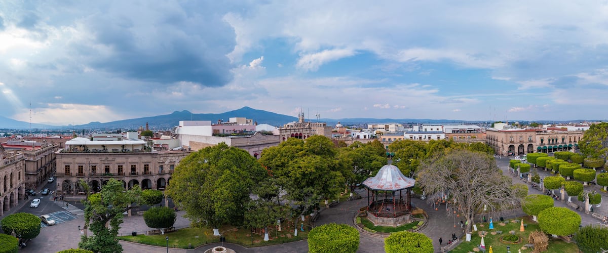 A cityscape with a prominent cathedral, a large plaza with a gazebo, and a mountain in the background.
