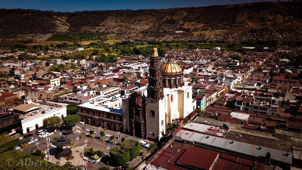 A cityscape with a prominent church featuring a golden dome and bell tower, surrounded by densely packed buildings and a hilly backdrop.