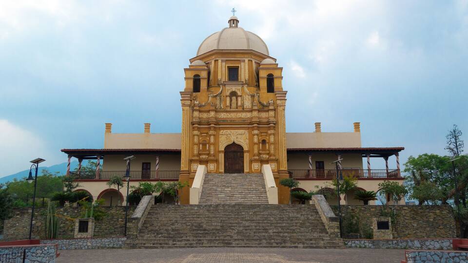 A historic church with a dome and bell towers, surrounded by stone steps and greenery.