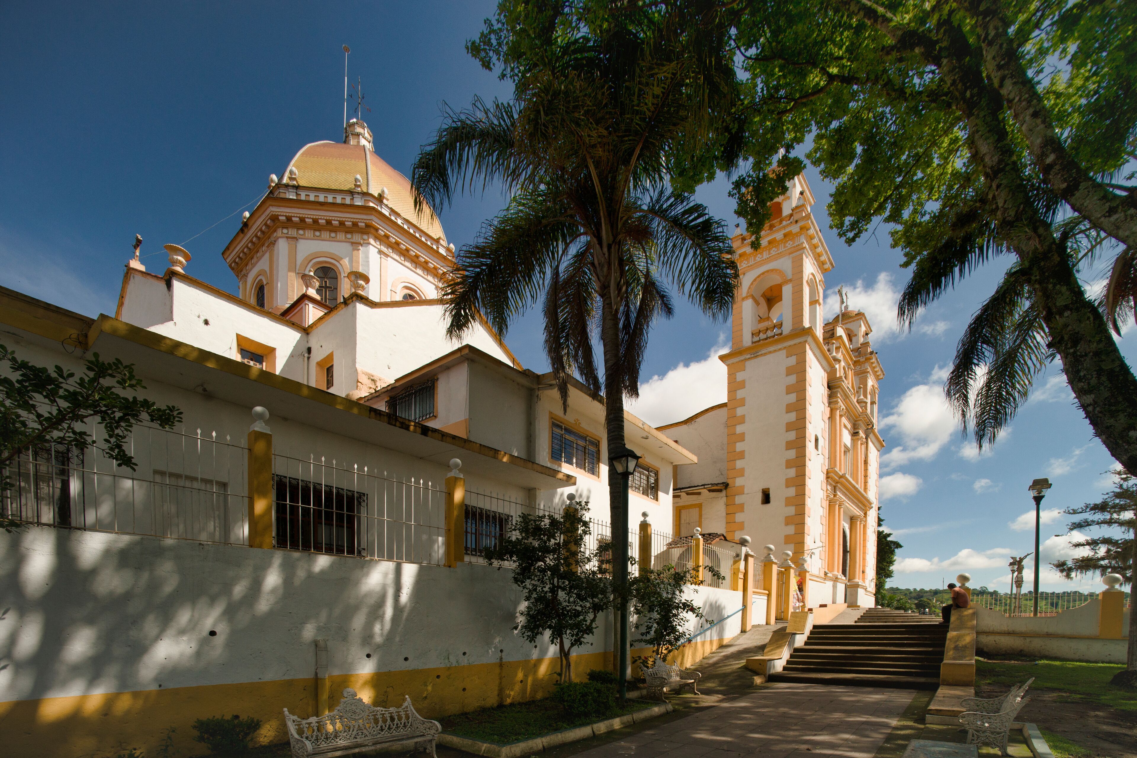 A historic building with a dome and bell tower, surrounded by palm trees and a clear sky.