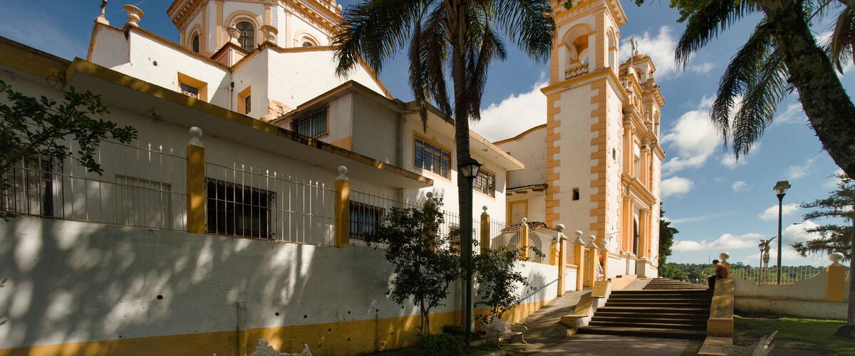 A historic building with a dome and bell tower, surrounded by palm trees and a clear sky.