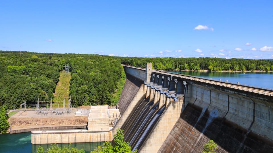 A large dam with multiple spillways and a river below.