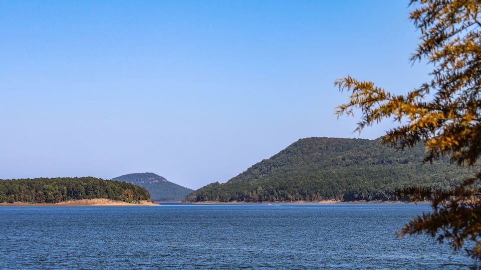 A calm lake with a forested island and a hill in the background.