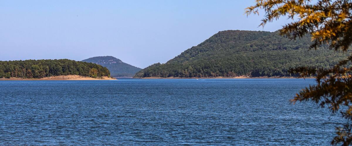 A calm lake with a forested island and a hill in the background.