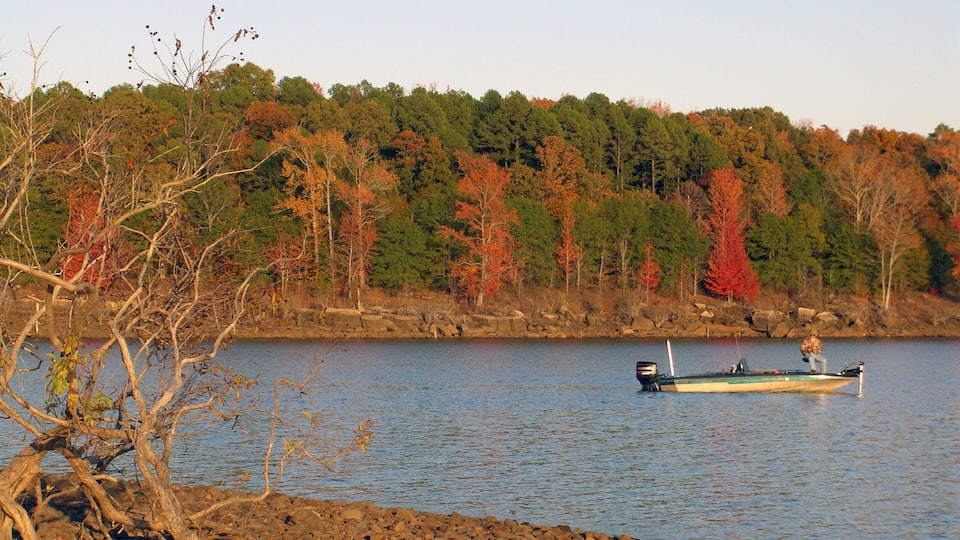 A lake with a boat on the water, surrounded by autumn-colored trees and rocky shoreline.