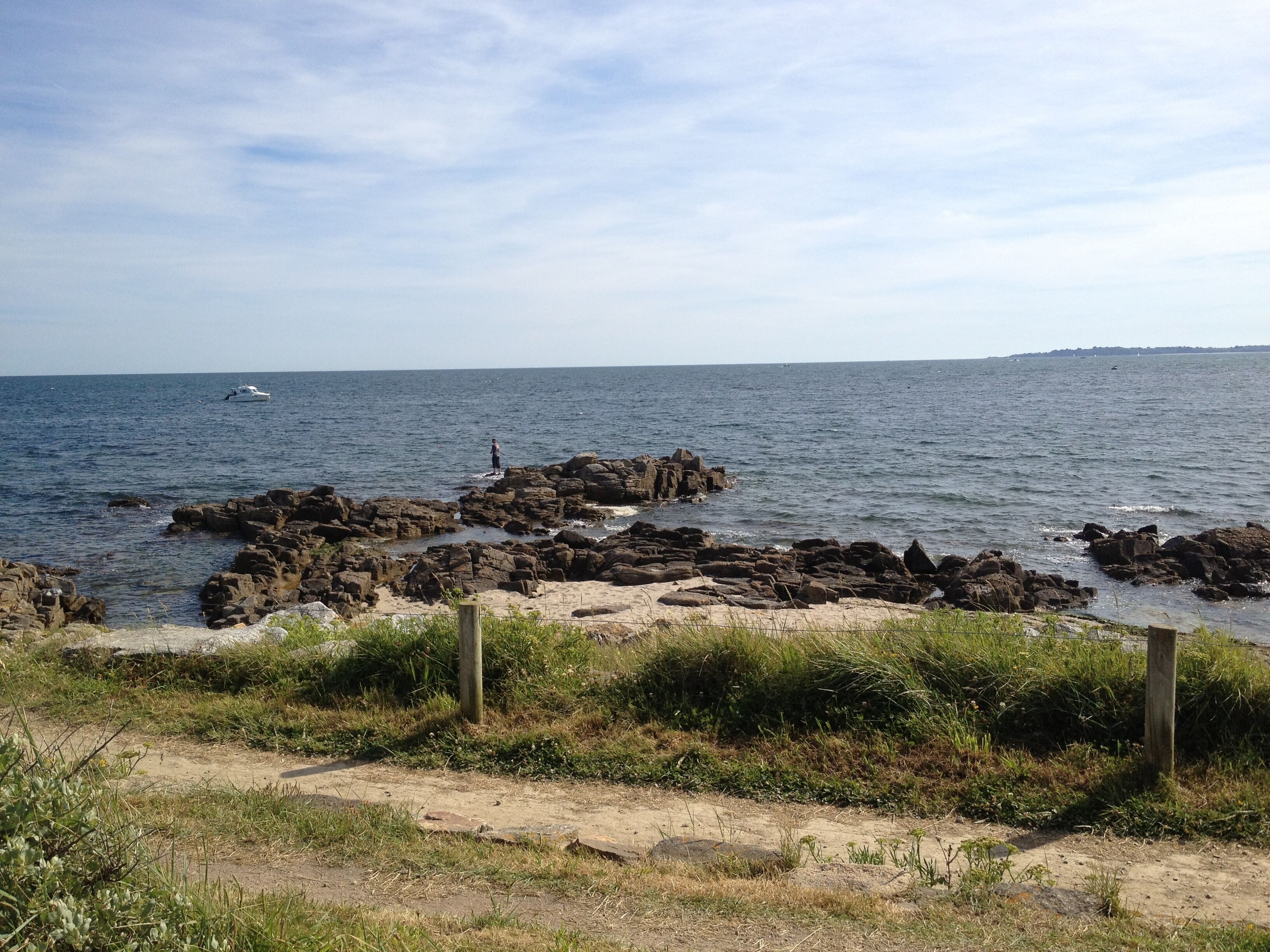 A rocky shoreline with a boat in the water and a person standing on the rocks.
