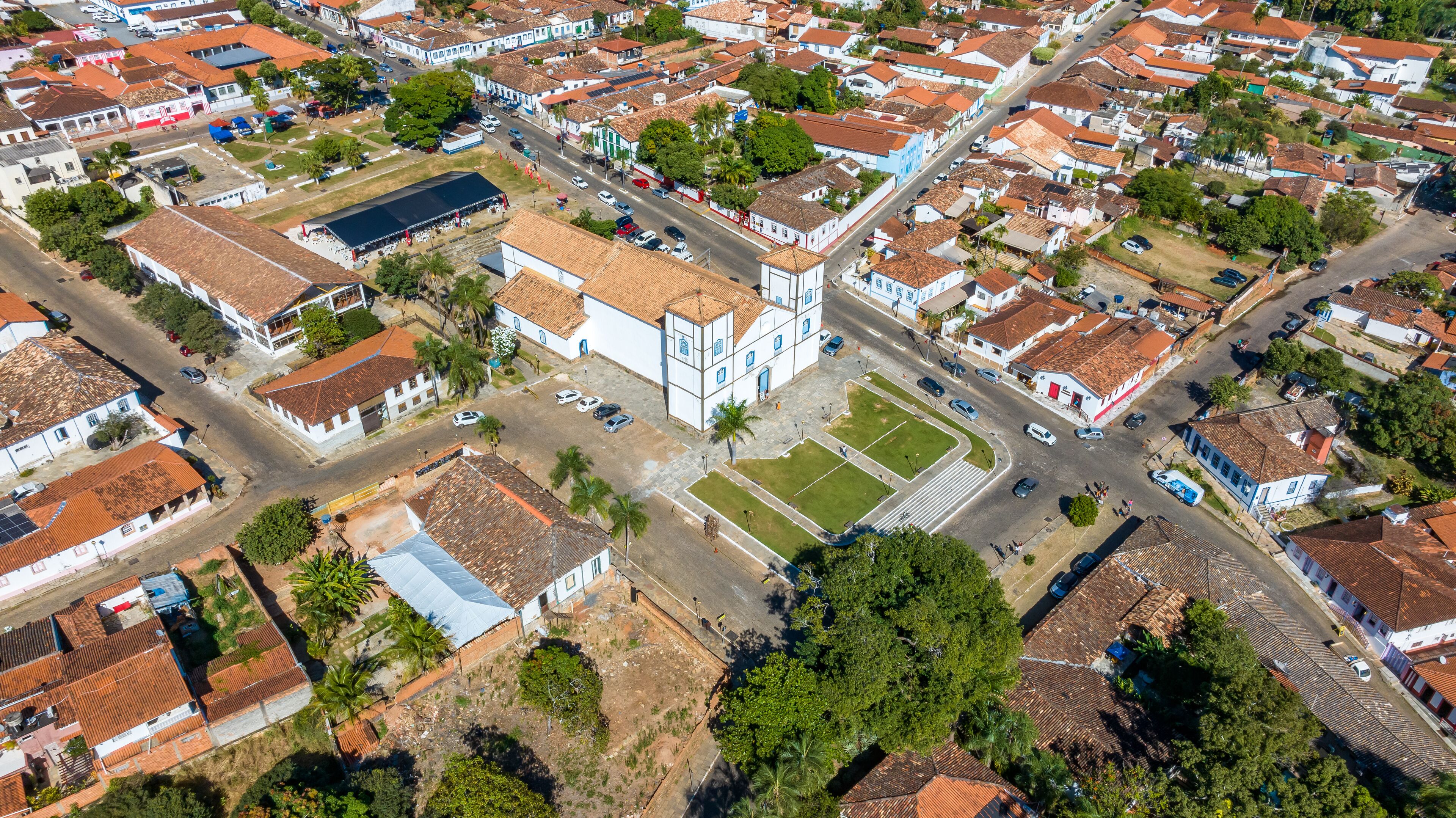An aerial view of a residential area with red-tiled roofs, white buildings, and a central plaza with a large open space and a few trees.