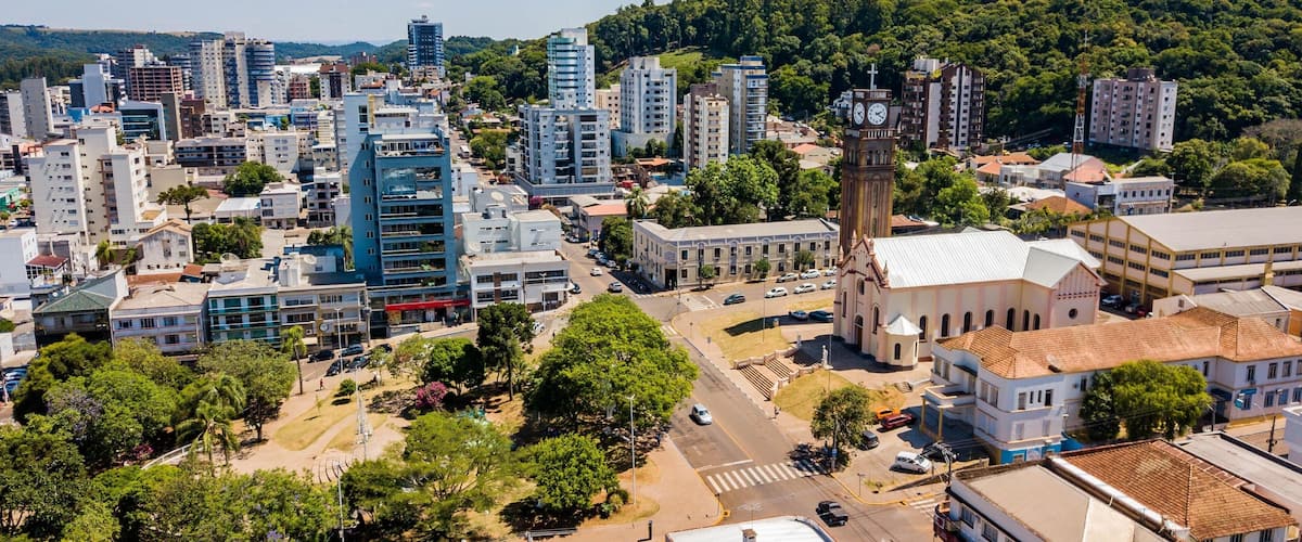 A cityscape with modern and historic buildings, a prominent clock tower, and a hilly backdrop.