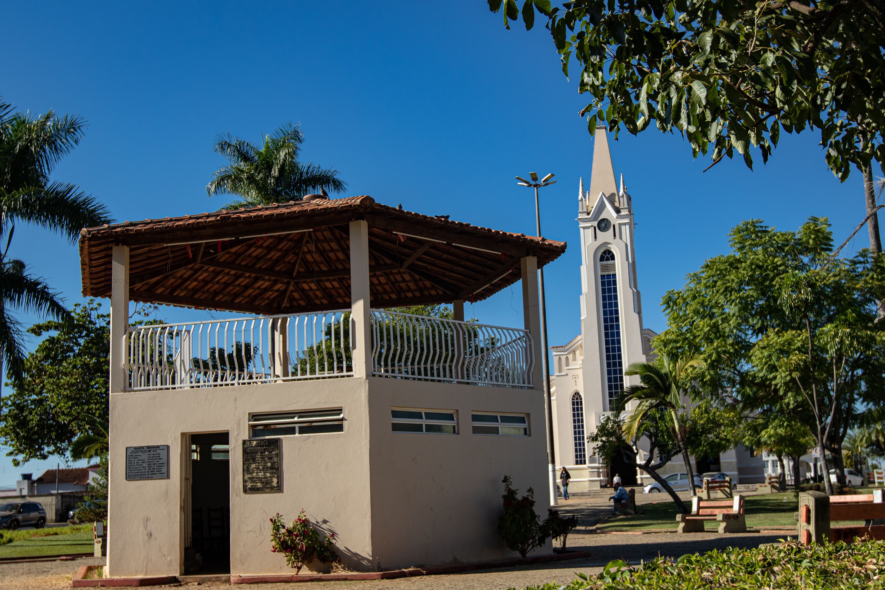 A small building with a balcony, a church with a tall steeple, and palm trees.