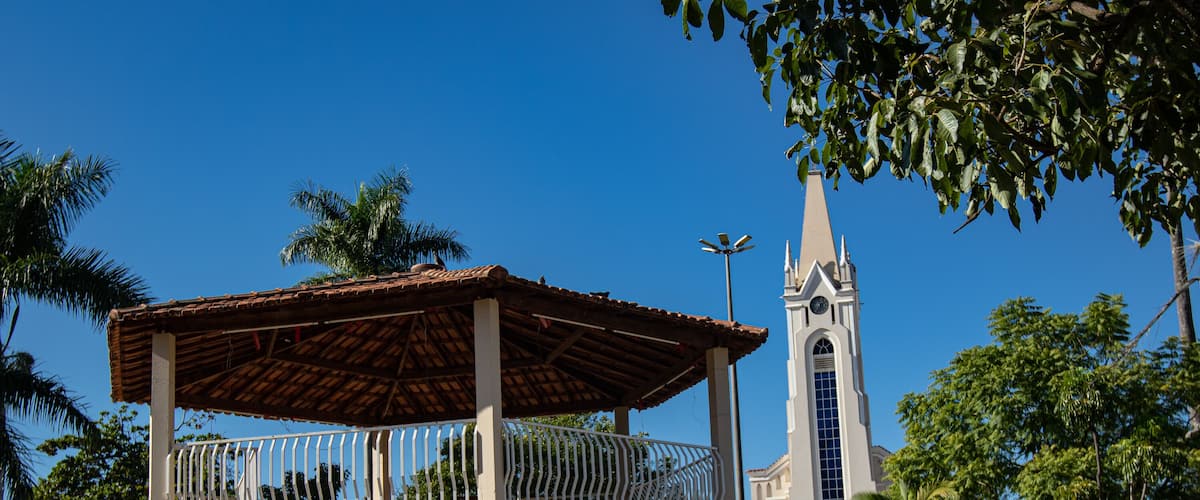 A small building with a balcony, a church with a tall steeple, and palm trees.