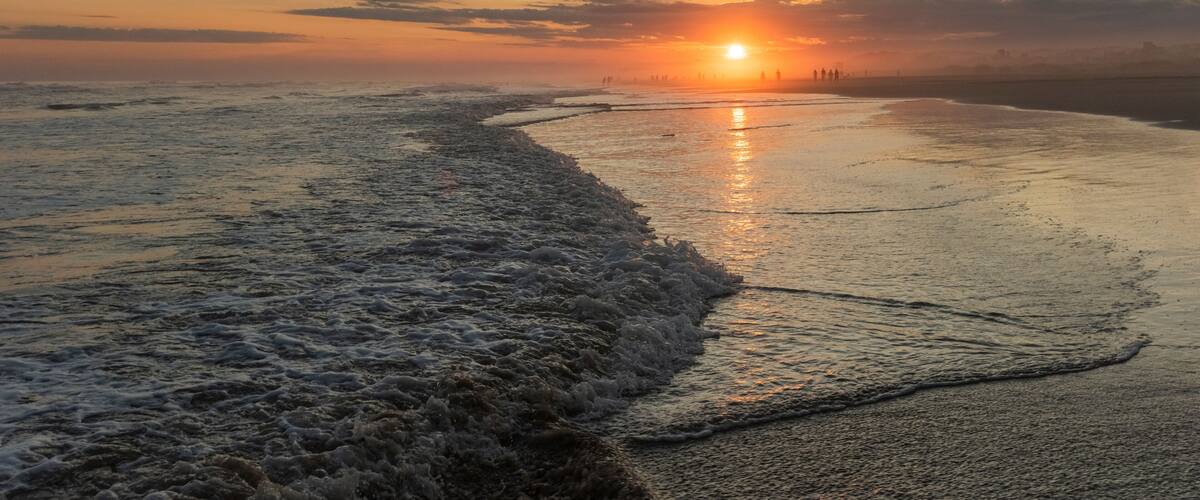 A beach at sunset with waves gently lapping the shore.