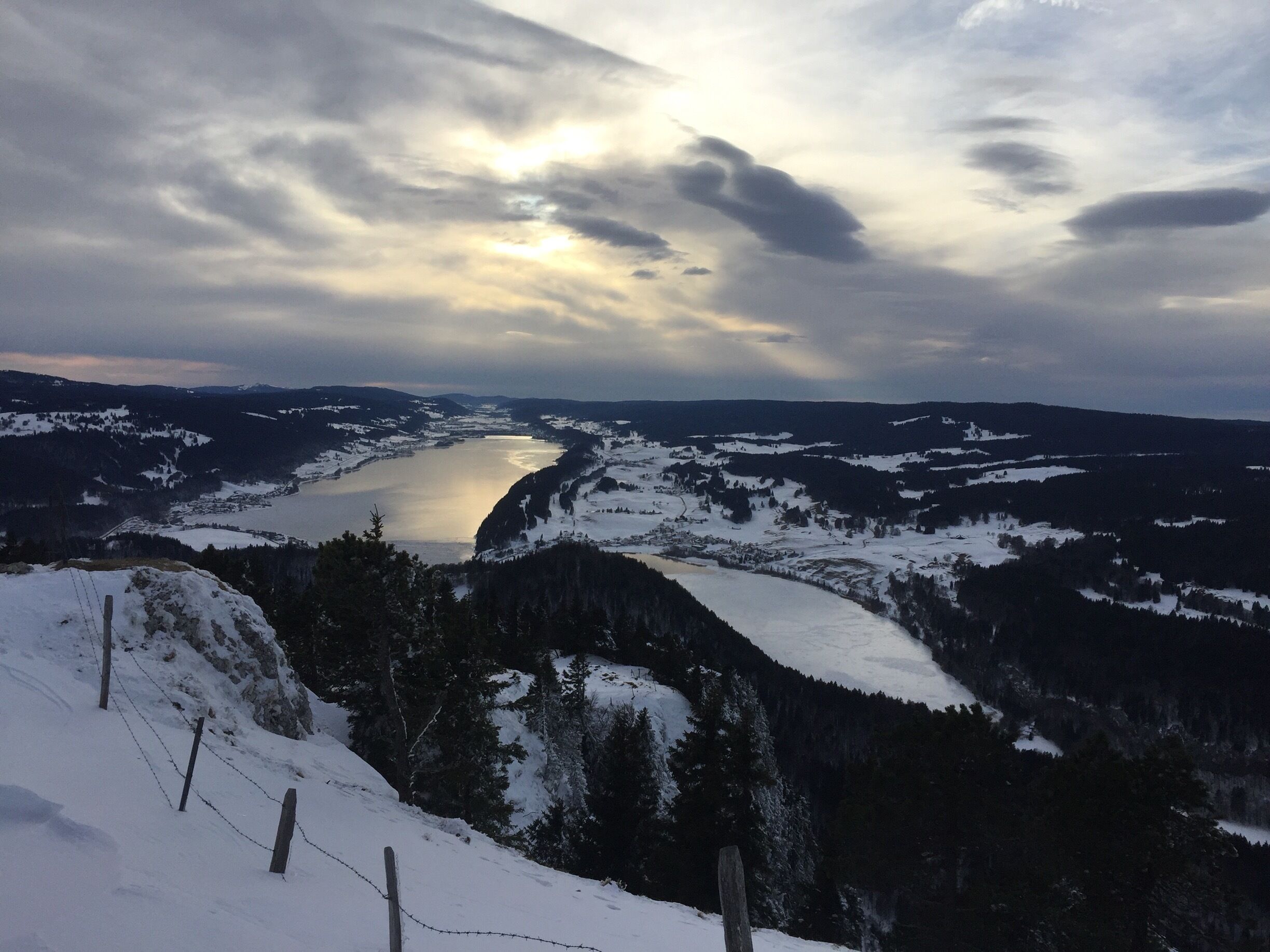 A snow-covered landscape with a river, mountains, and a cloudy sky.
