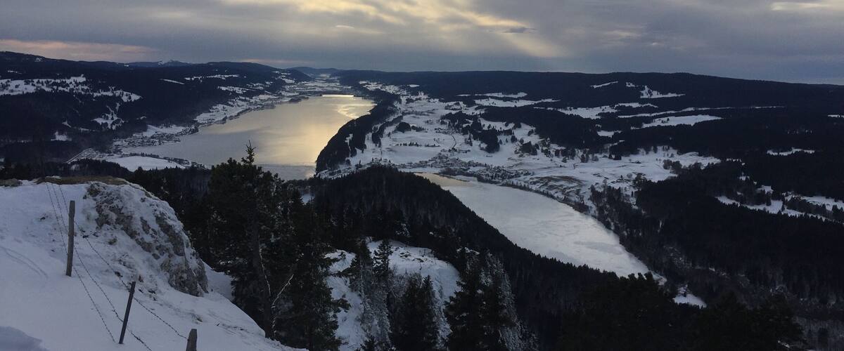 A snow-covered landscape with a river, mountains, and a cloudy sky.