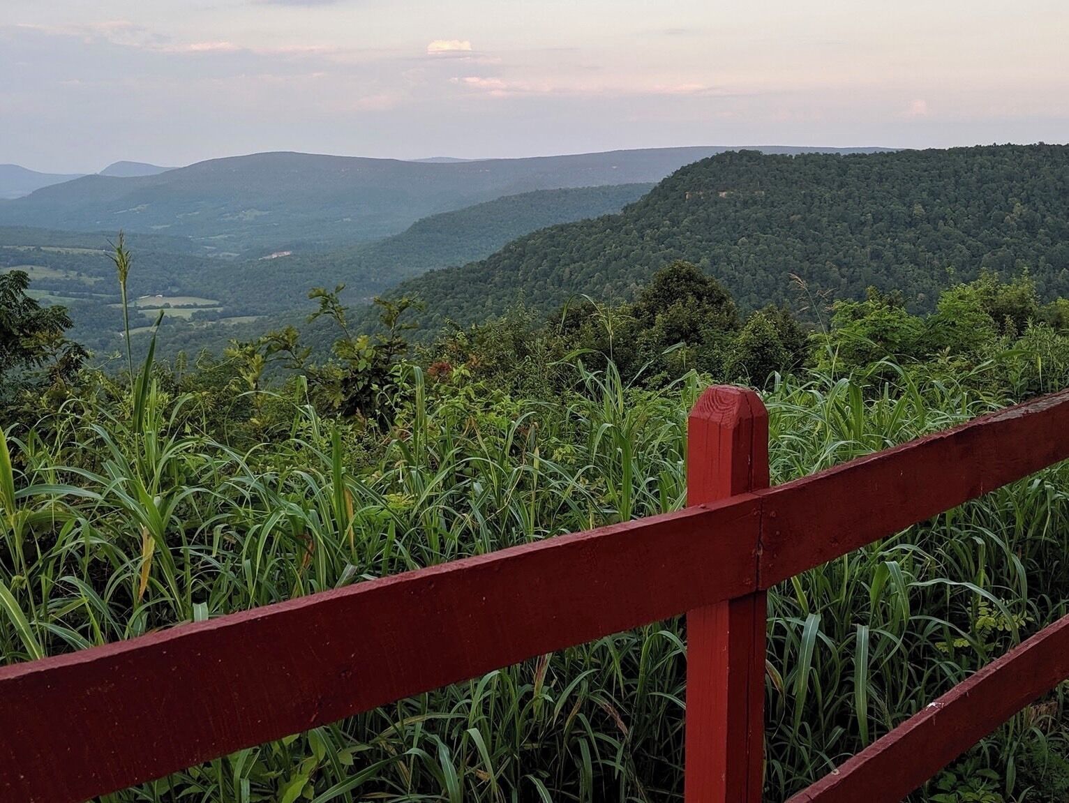 A red wooden fence overlooking a lush green valley with distant hills.