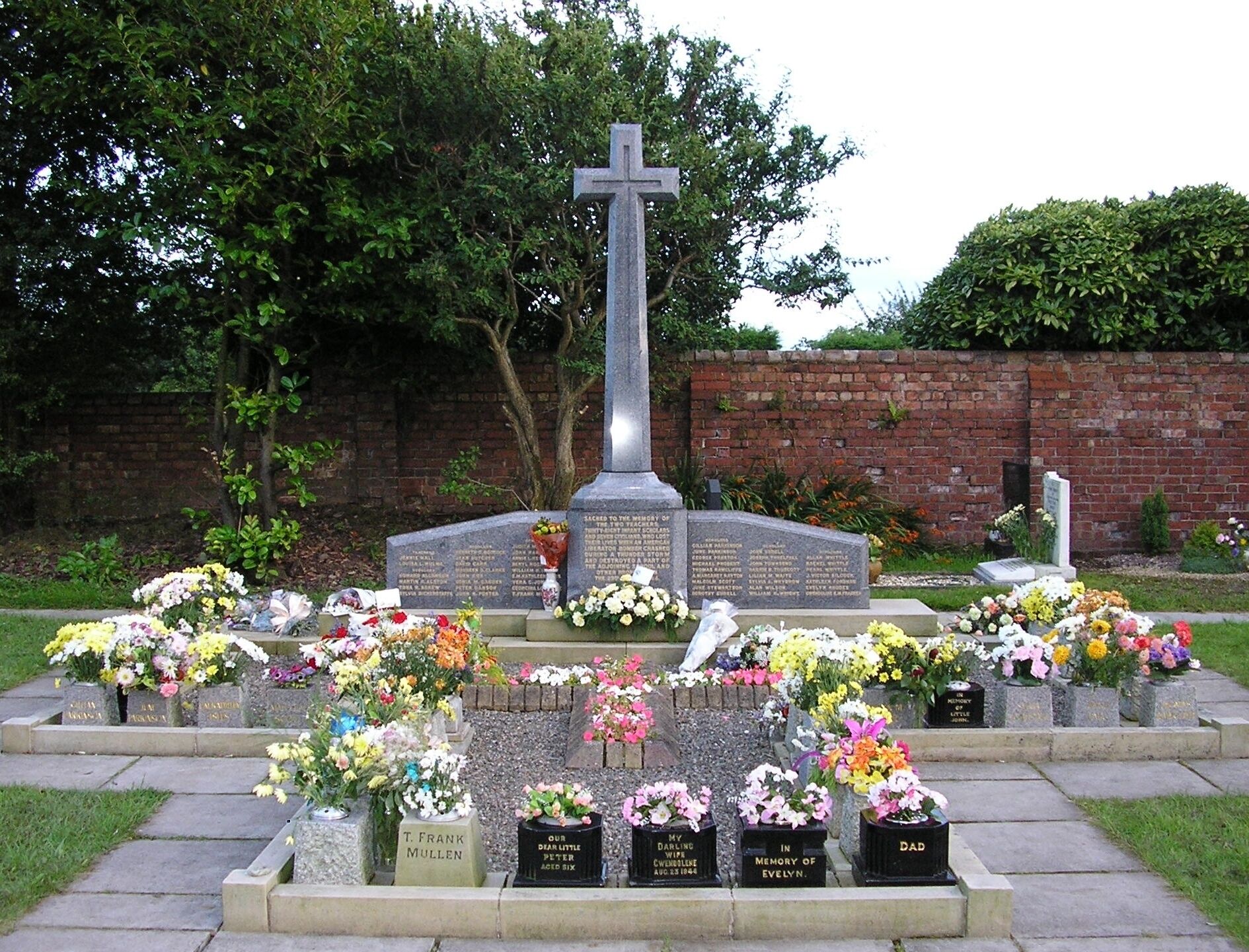 A cemetery with a prominent cross monument surrounded by graves adorned with flowers.