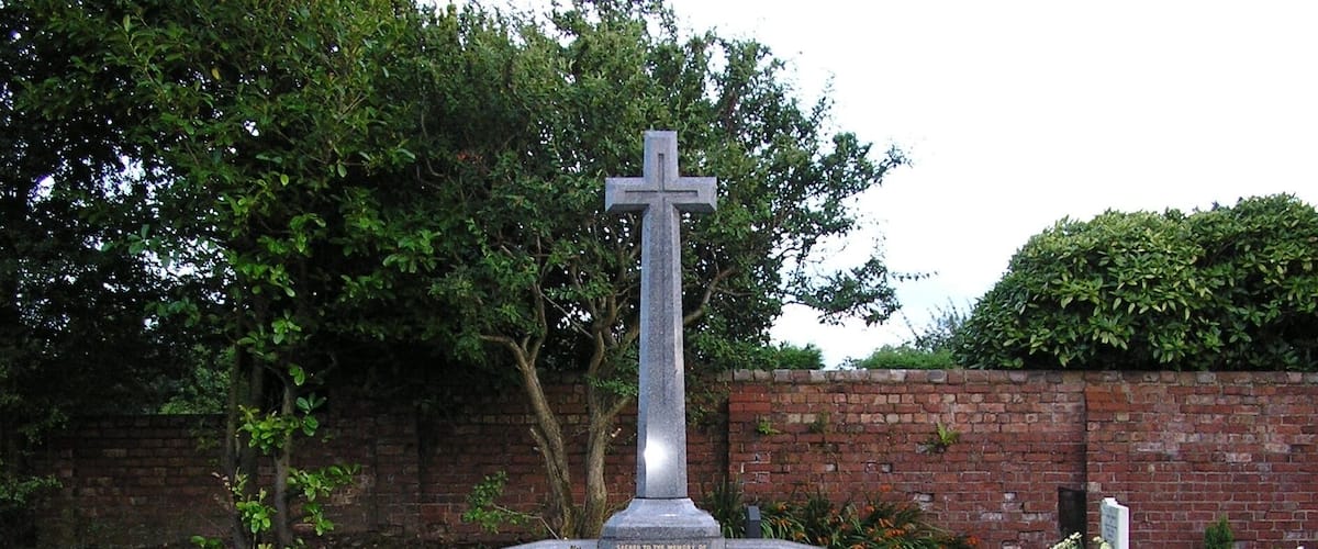 A cemetery with a prominent cross monument surrounded by graves adorned with flowers.