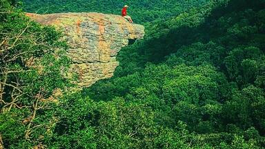 A person sitting on a rock ledge overlooking a dense forest.