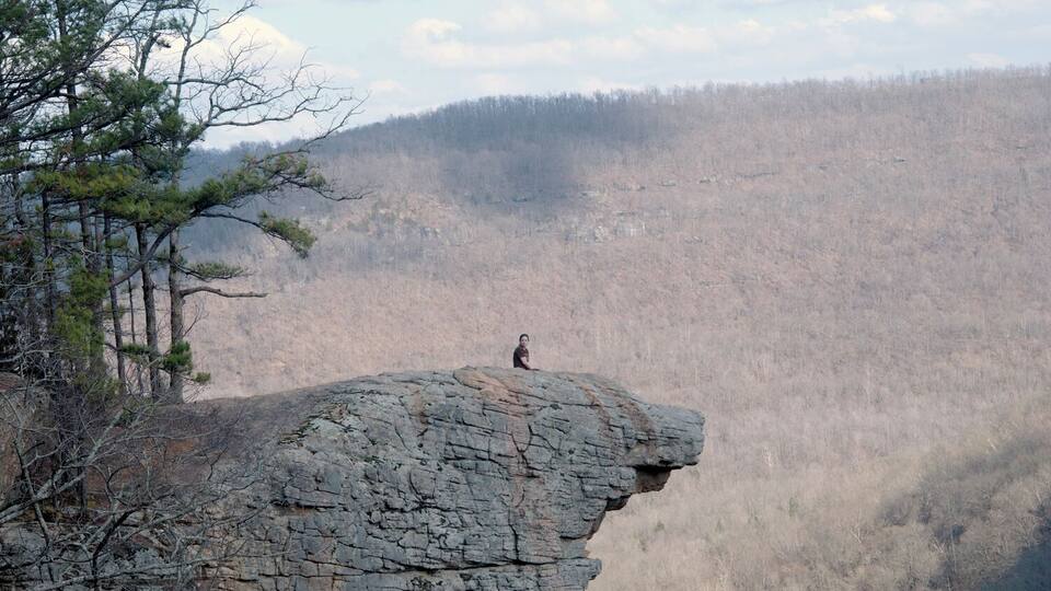 A person standing on a rocky cliff overlooking a forested valley.