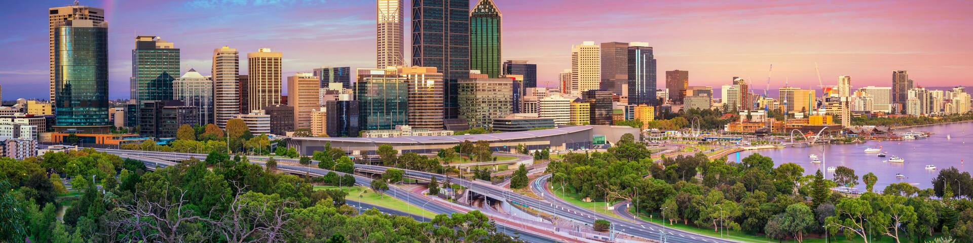A city skyline with modern skyscrapers, a river with boats, and a highway with greenery.