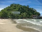 A beach with waves, a forested hill, and a building with 'ANGKAWI ATAKEDAH' written on it.
