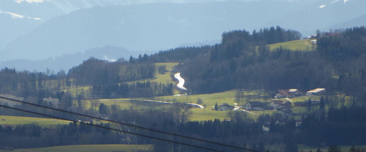 A mountainous landscape with a winding road, green fields, and scattered houses.