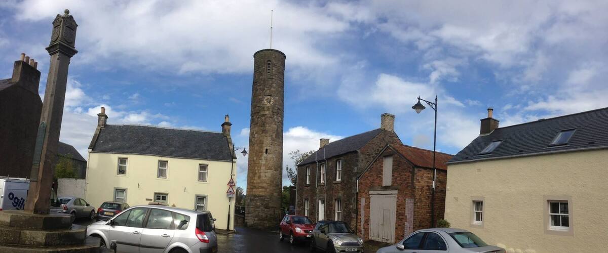 A street with historic buildings, a clock tower, and parked cars.