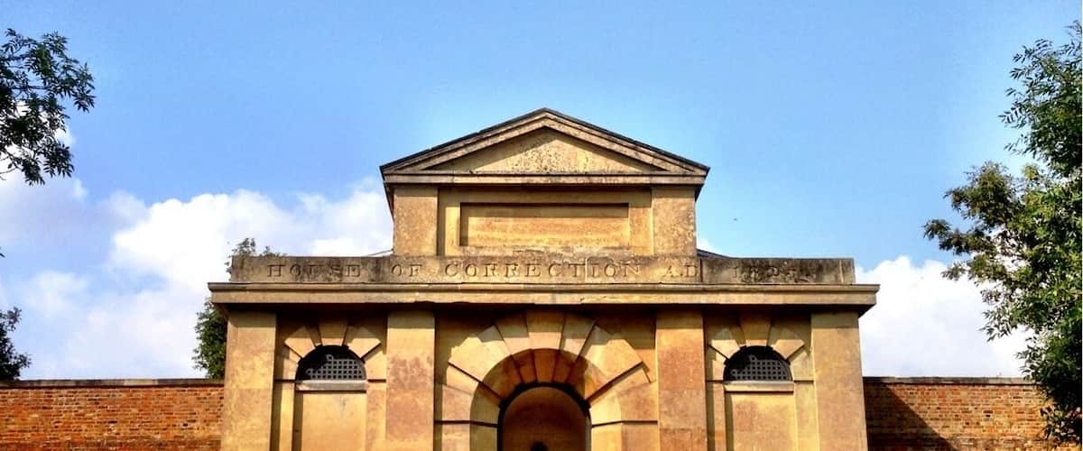 A historic building with a central archway and a triangular pediment, surrounded by brick walls and greenery.